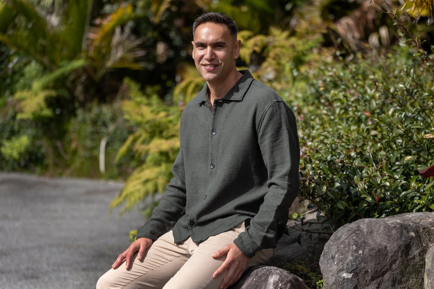 Riki Hoeata seated beside garden stones and greenery.